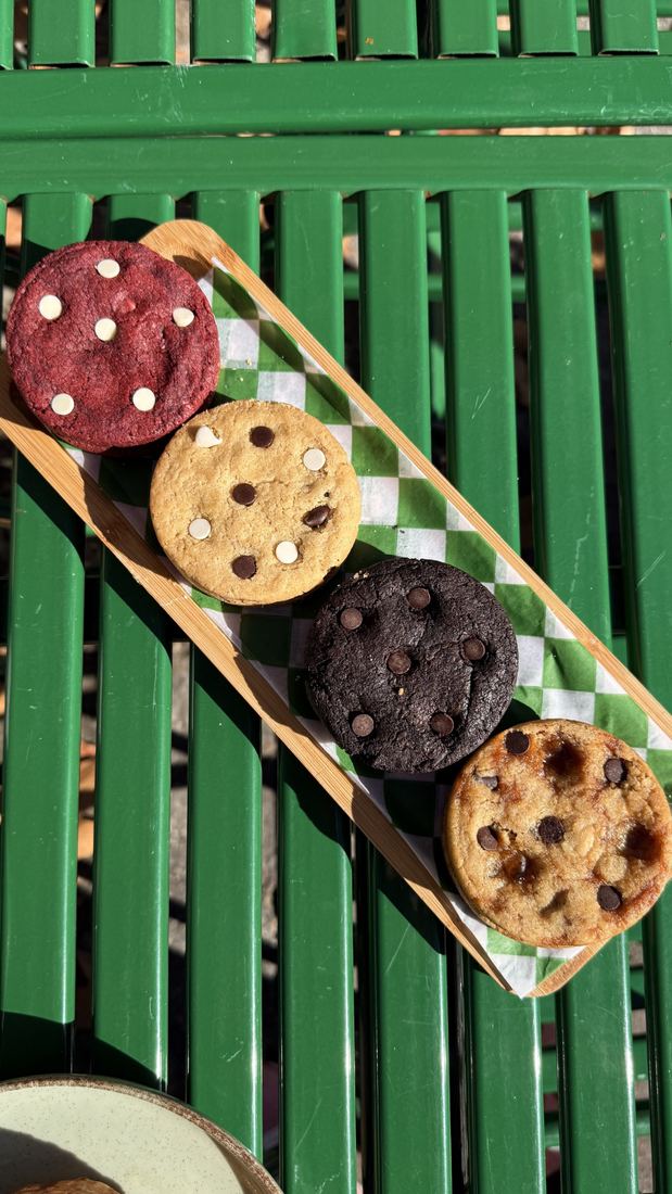 Cuatro cookies alineadas sobre una tabla, delante de una reja verde.